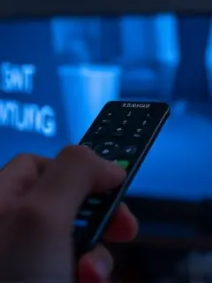 Mão segurando o controle remoto diante da TV