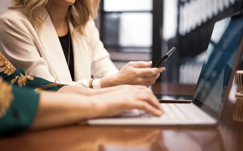 Mulher com celular e notebook no escritório
